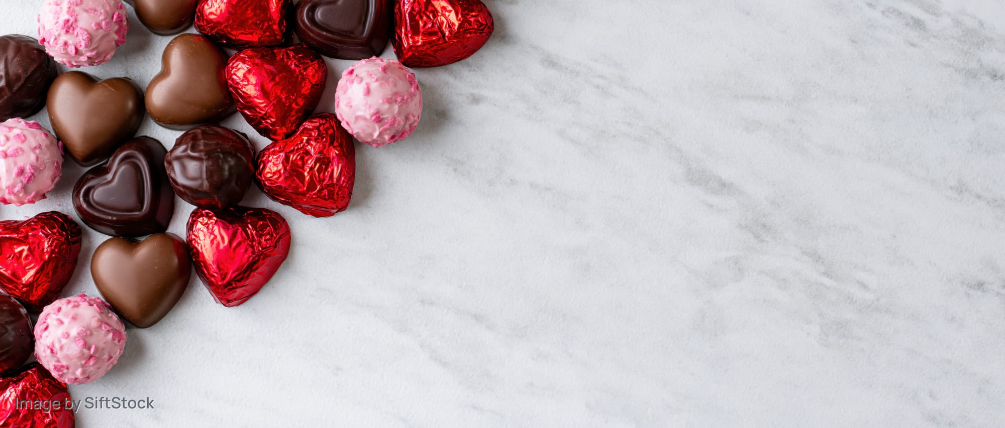 Heart-shaped chocolates scattered in corner on marble surface with copyspace