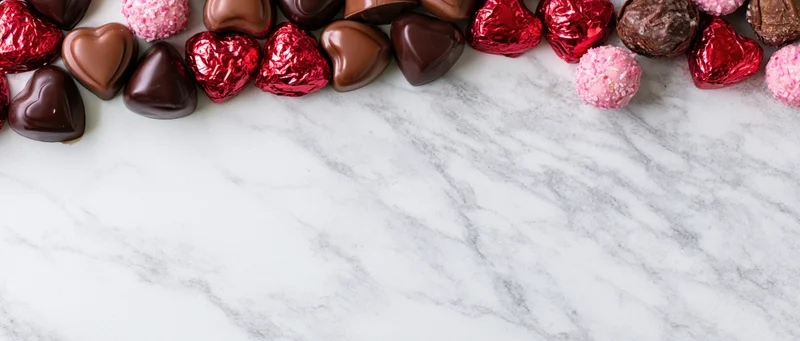 Heart-shaped chocolates and candy arranged along the top of a marble surface with copyspace below