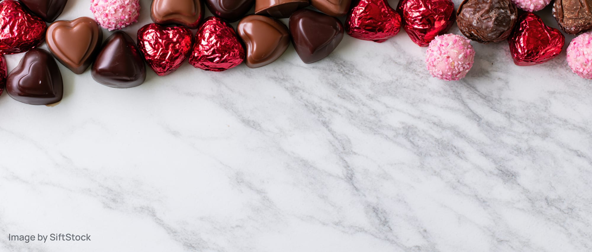 Heart-shaped chocolates and candy arranged along the top of a marble surface with copyspace below