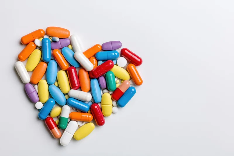 Colorful pills and capsules arranged in heart shape on white background