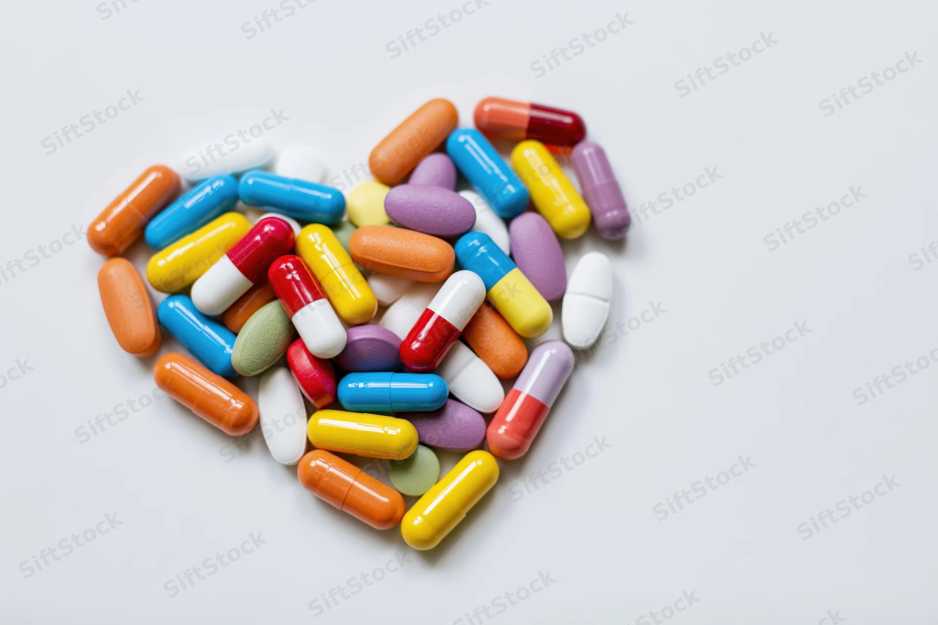 Colorful pills and capsules arranged in heart shape on white surface