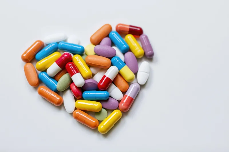 Colorful pills and capsules arranged in heart shape on white surface
