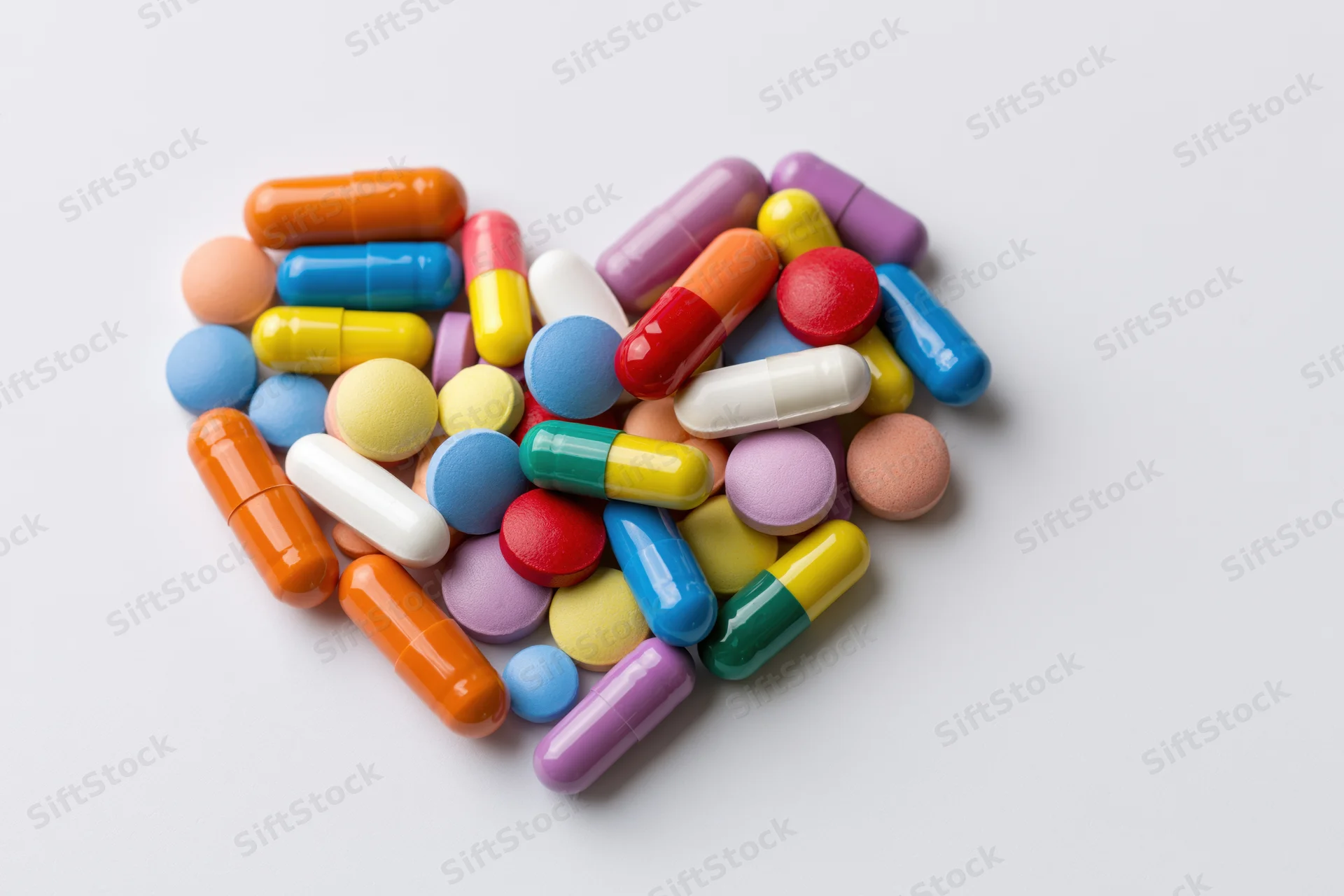 Colorful pills and capsules arranged in heart shape on white background