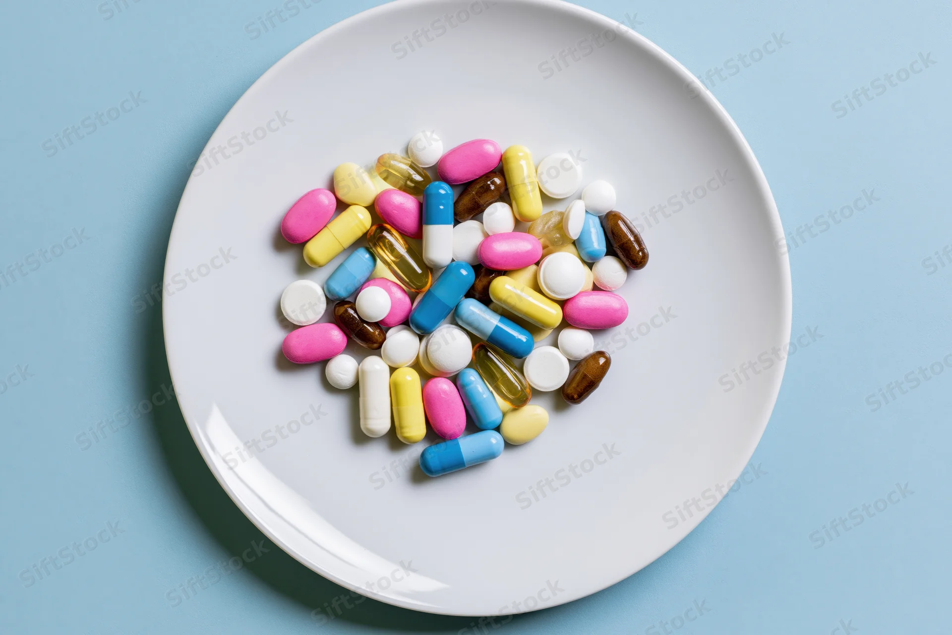 Assorted colorful pills and capsules scattered on a white plate against a blue background