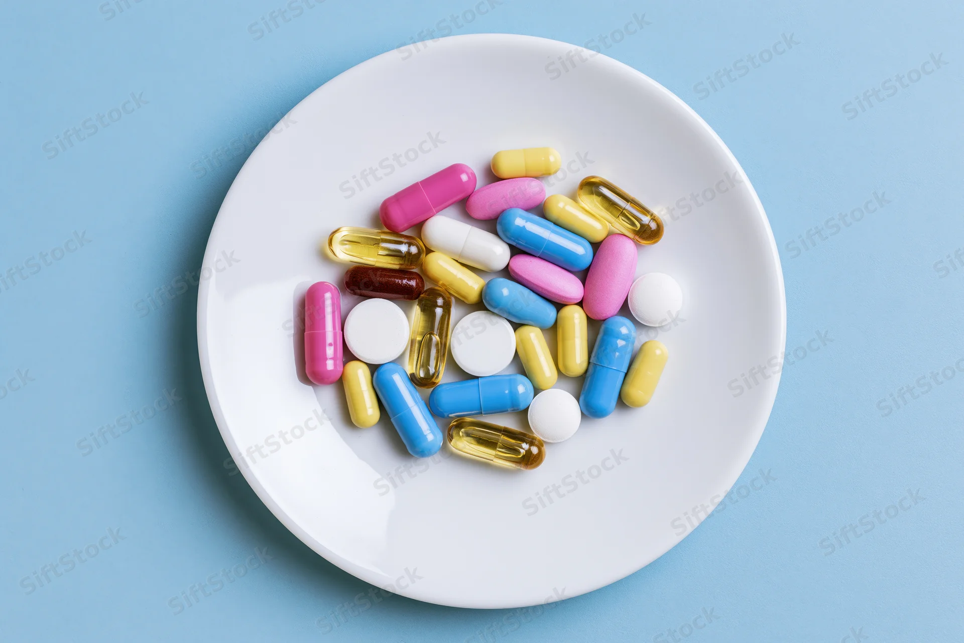 Colorful pills and capsules scattered on a white plate against a blue background