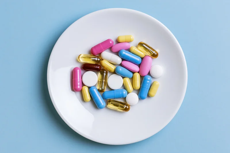Colorful pills and capsules scattered on a white plate against a blue background