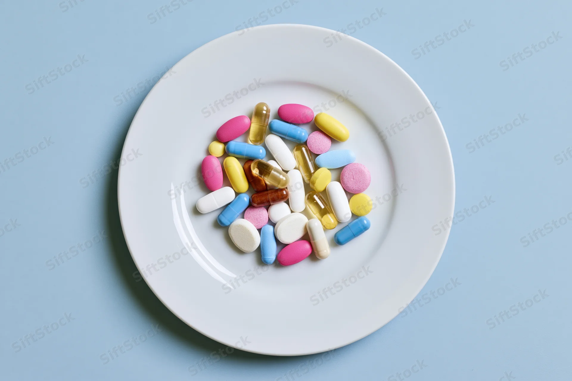 Colorful pills and capsules scattered on a white plate against a blue background