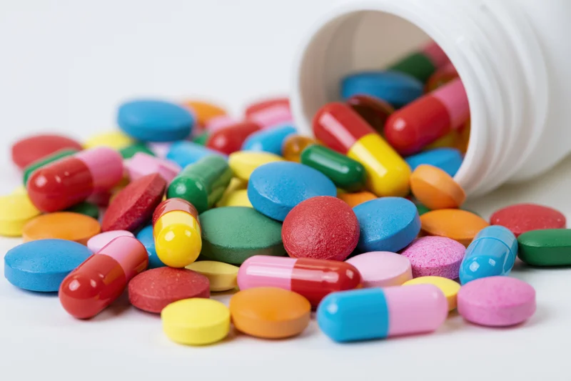 Colorful pills and capsules spilled from a white bottle on a plain surface