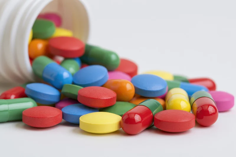 Colorful pills and capsules spilled from a white bottle onto a plain surface