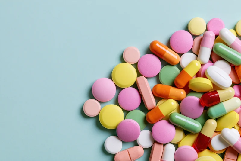 Colorful pills and capsules scattered on a blue background with copyspace on the left