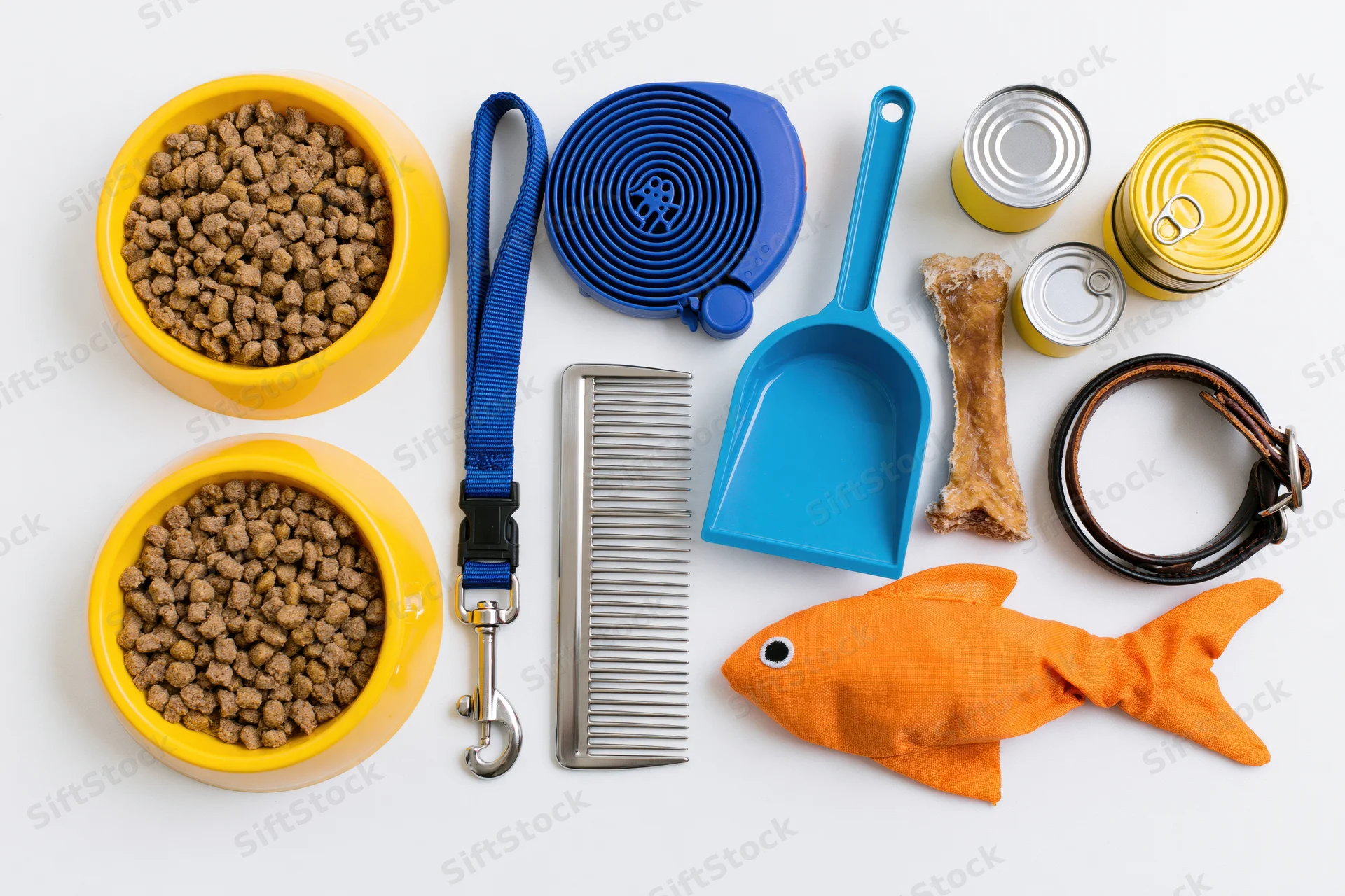 Pet supplies arranged flat lay on white background including bowls, leash, collar, toy, comb, scoop, cans, and kibble