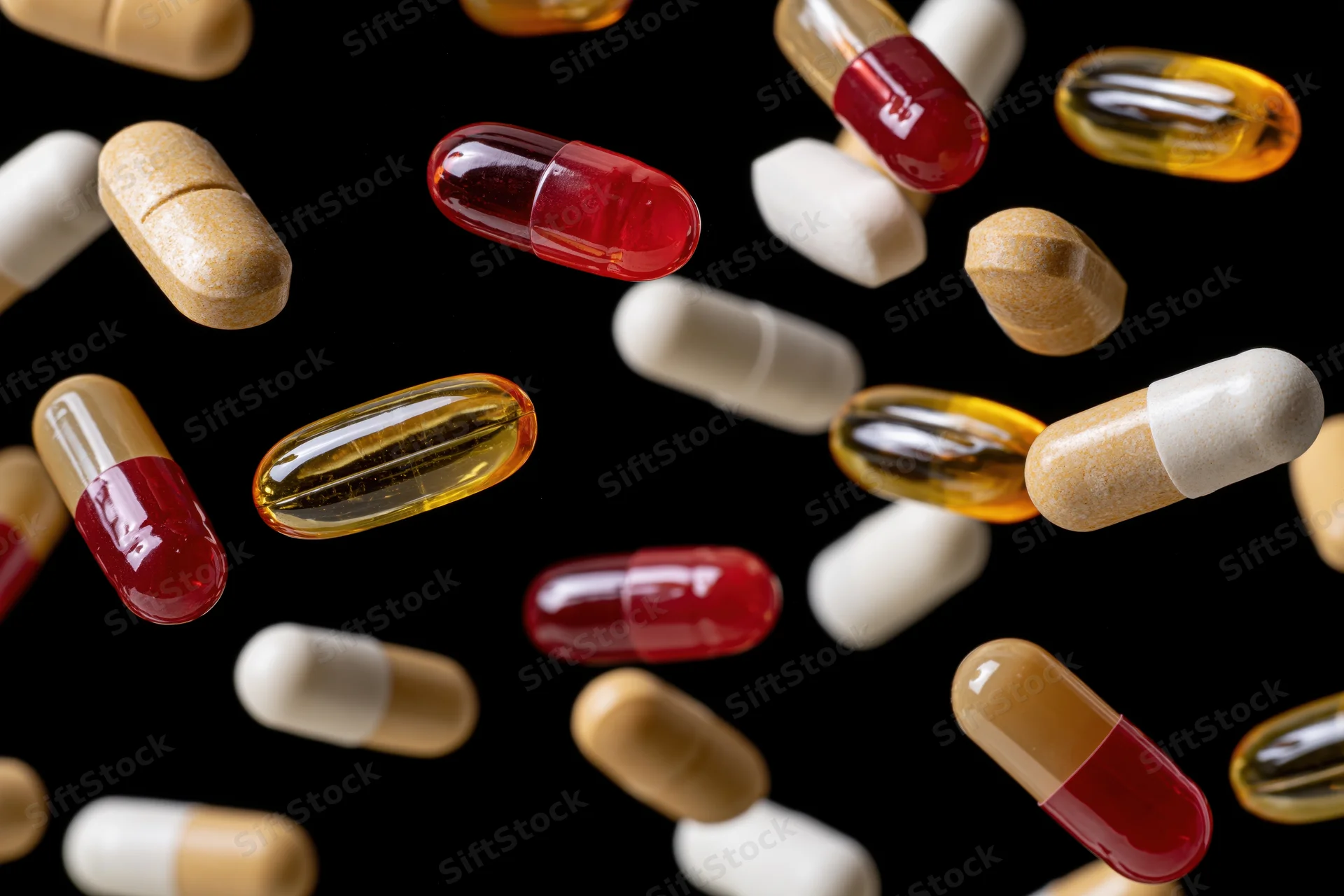 Assorted pharmaceutical capsules and gel pills suspended mid-air against black background
