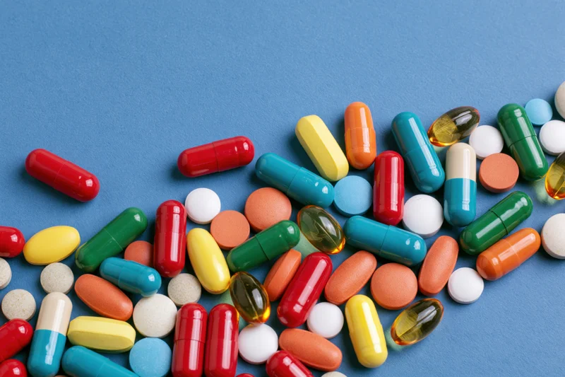 Assorted pharmaceutical capsules tablets and softgels scattered on blue background