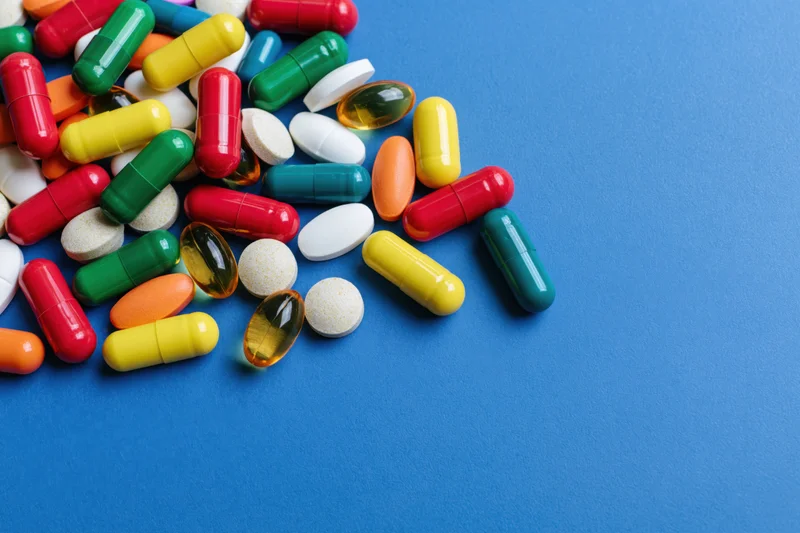 Assorted pharmaceutical capsules tablets and softgels scattered on blue surface with copyspace