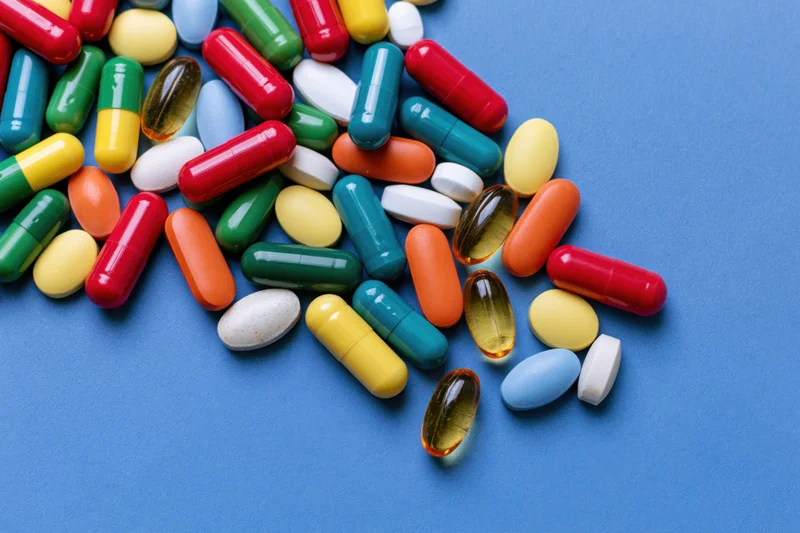 Assorted pharmaceutical capsules tablets and softgels scattered on blue surface