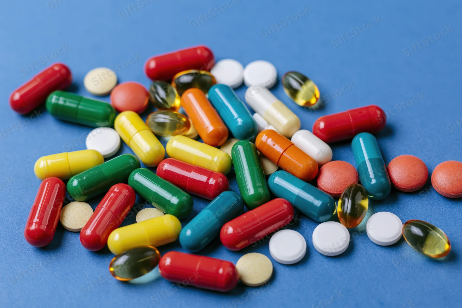 Assorted pharmaceutical capsules tablets and gel softgels scattered on blue surface