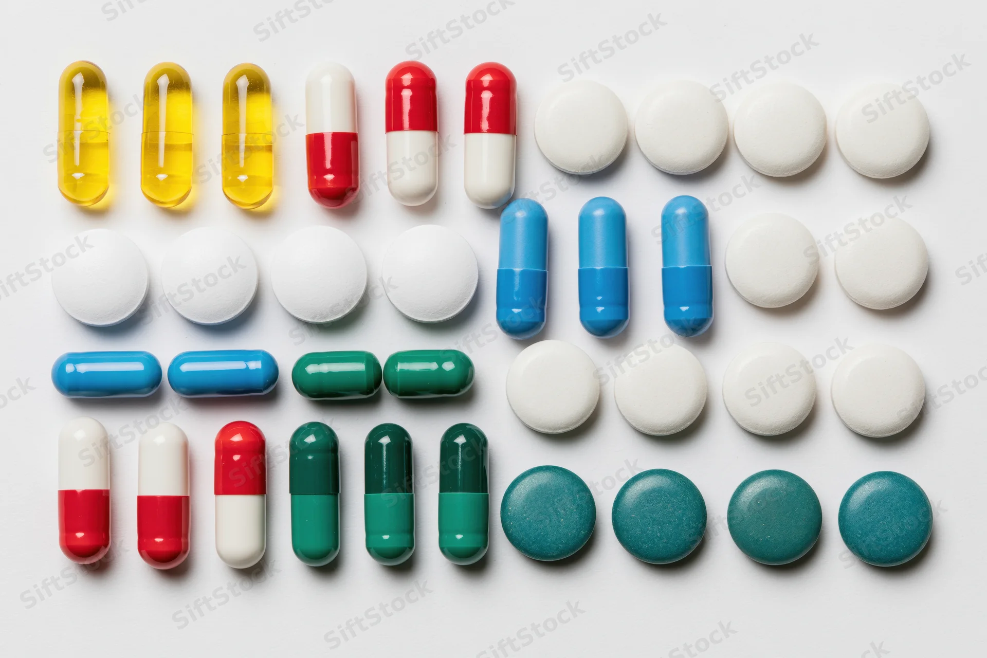 Assorted pharmaceutical pills and capsules arranged in rows on white background