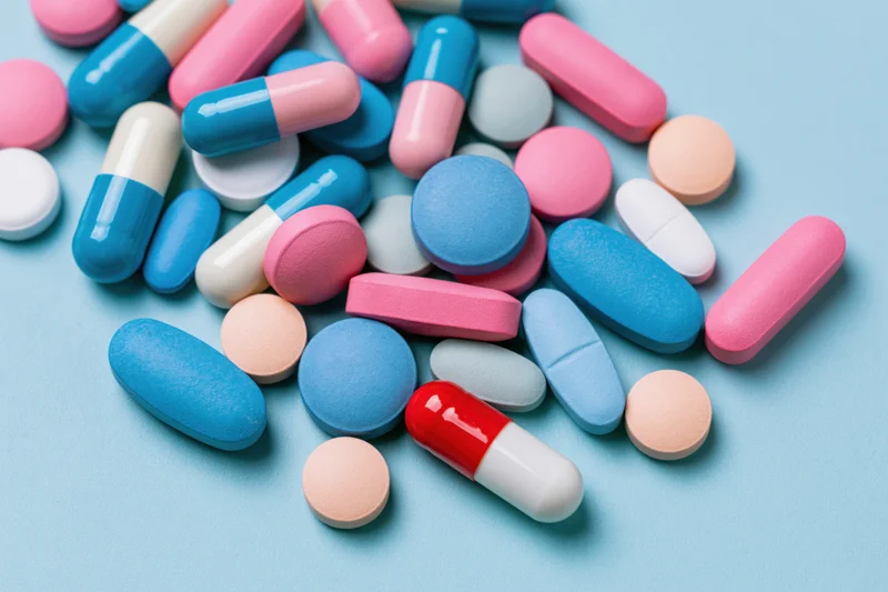 Assorted pharmaceutical pills and capsules scattered on a light blue surface