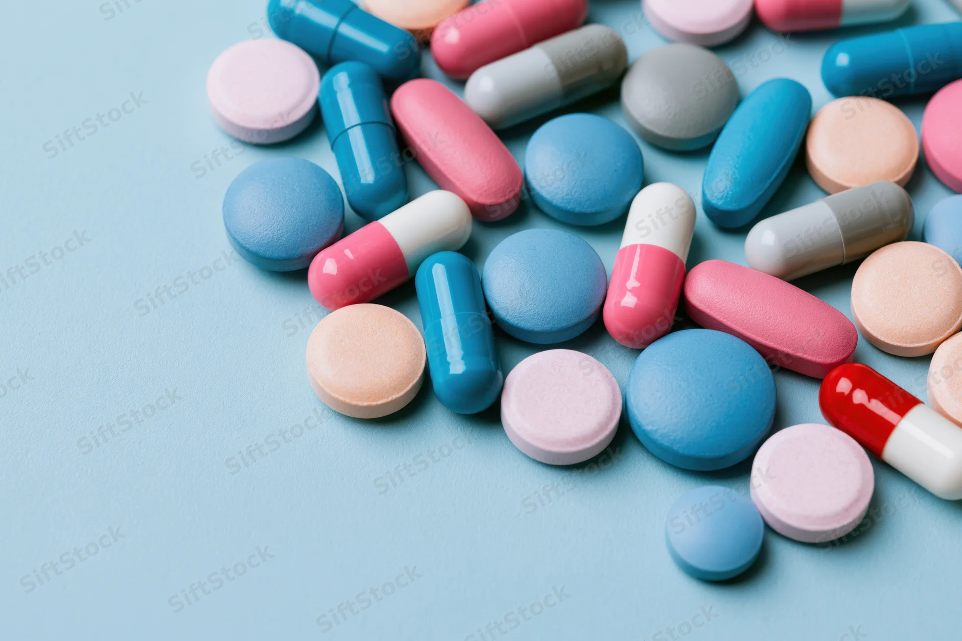 Assorted pharmaceutical pills and capsules scattered on a light blue surface