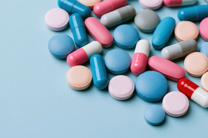 Assorted pharmaceutical pills and capsules scattered on a light blue surface