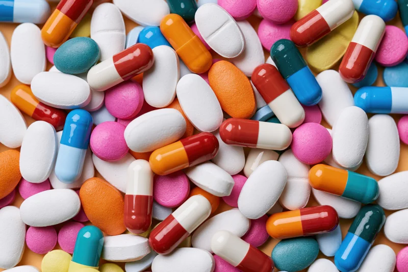 Assorted pharmaceutical pills and capsules scattered across a surface in a close-up flat lay view
