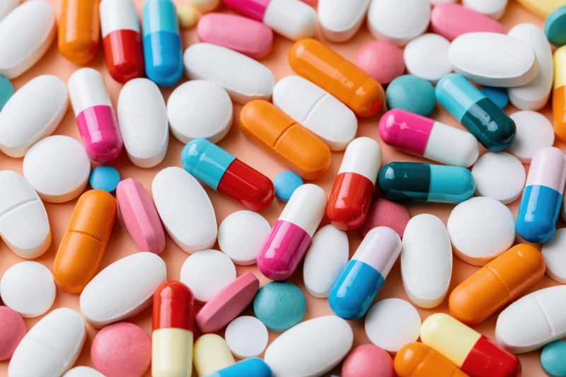 Assorted pharmaceutical pills and capsules scattered across a surface