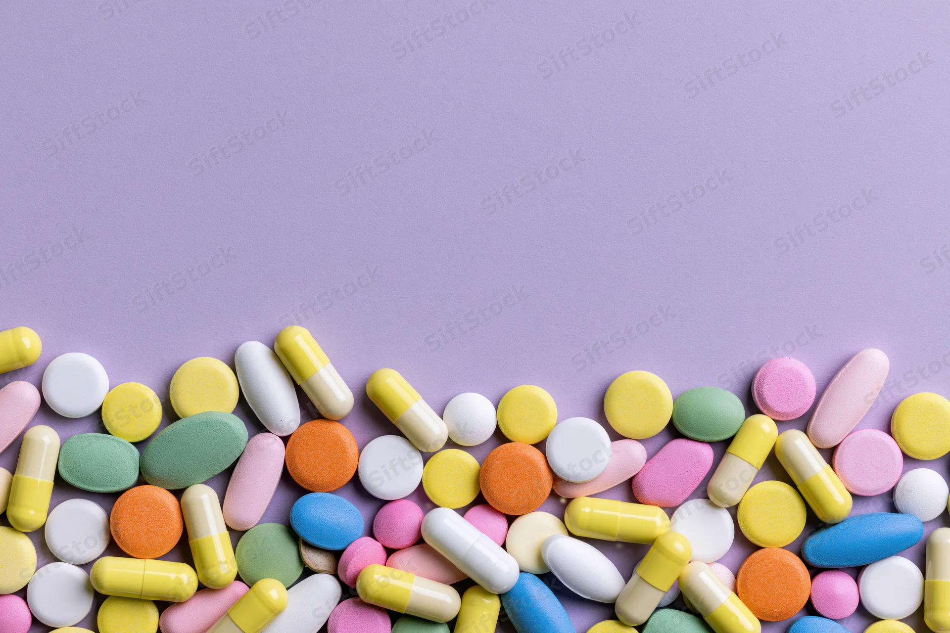 Assorted pharmaceutical pills and capsules scattered across a purple surface with copyspace above