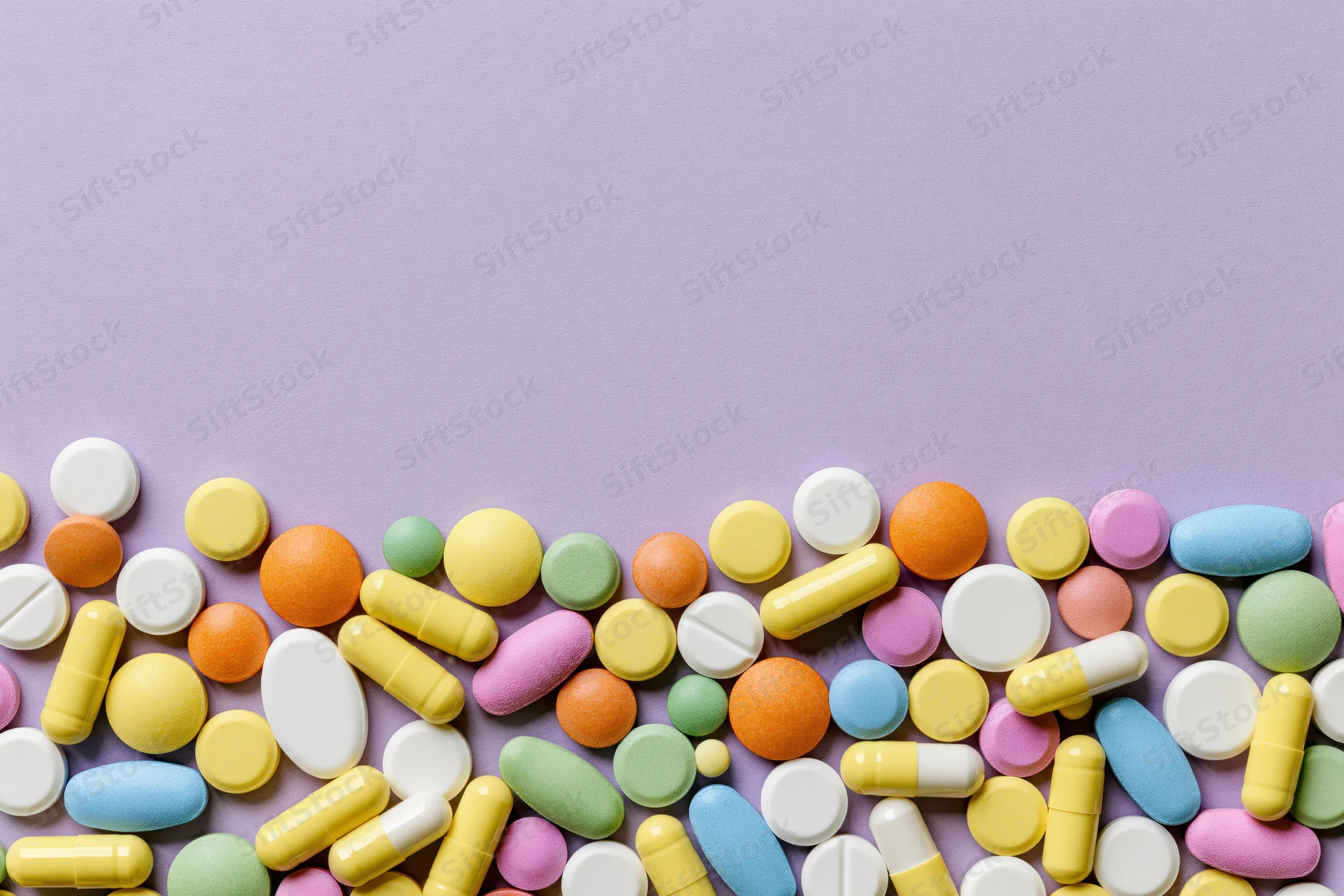 Assorted pharmaceutical pills and capsules scattered across a purple surface in a flat lay arrangement