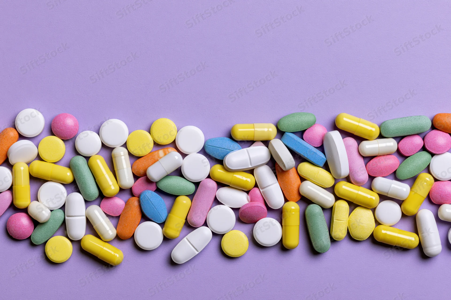 Assorted pharmaceutical pills and capsules scattered across a purple surface with copyspace above