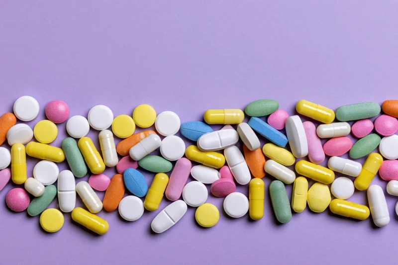 Assorted pharmaceutical pills and capsules scattered across a purple surface with copyspace above