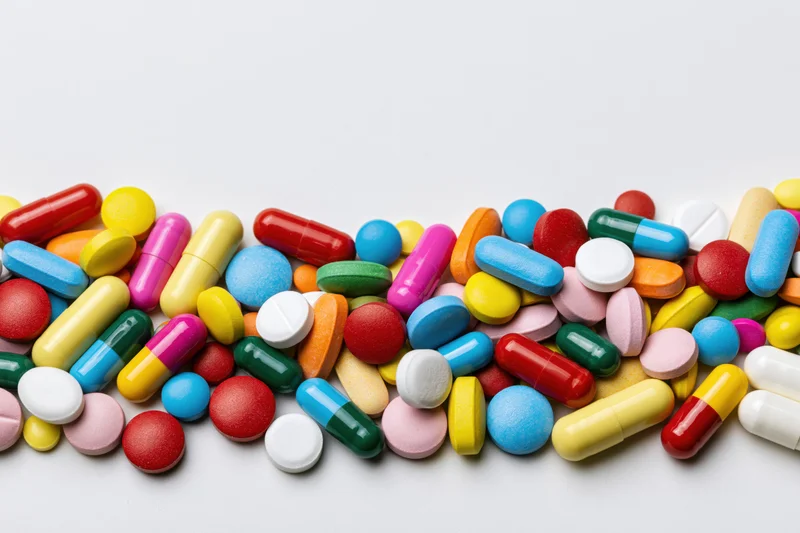 Assorted colorful pills and capsules scattered across a white surface
