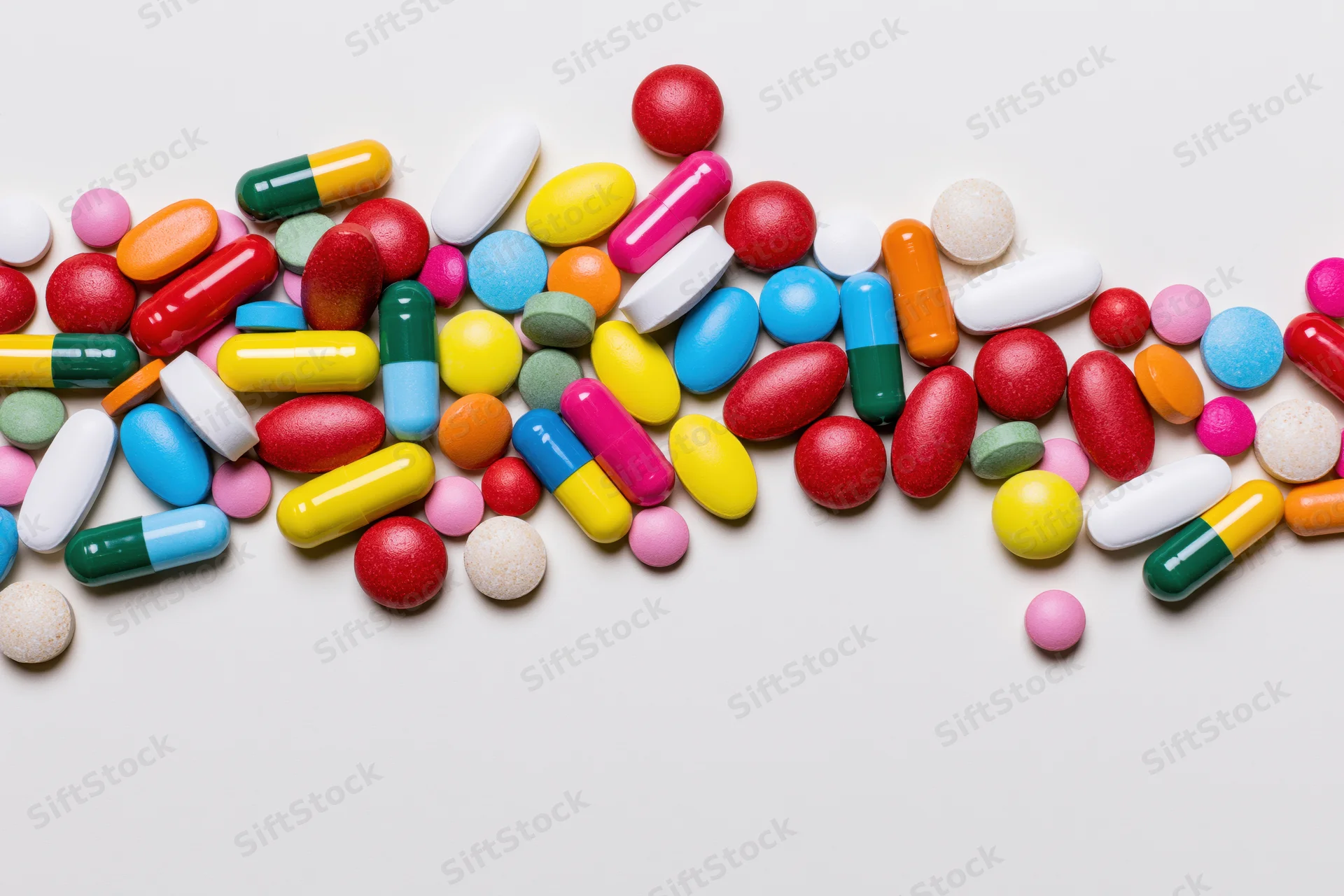 Assorted pharmaceutical pills and capsules scattered loosely on white surface with copyspace