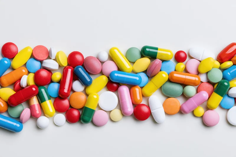 Assorted colorful pharmaceutical pills and capsules scattered loosely on white surface