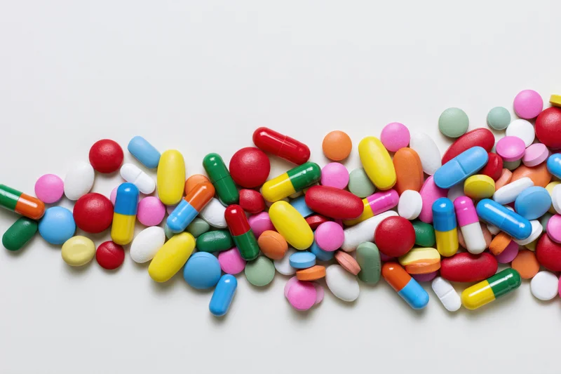 Assorted colorful pills and capsules scattered loosely on white background