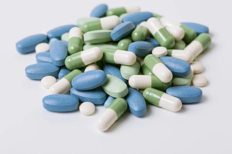Assorted pharmaceutical pills and capsules scattered loosely on a white surface