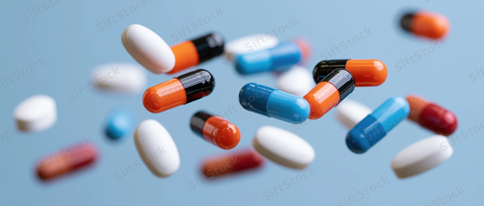 Assorted pharmaceutical pills and capsules floating mid-air against a blue background