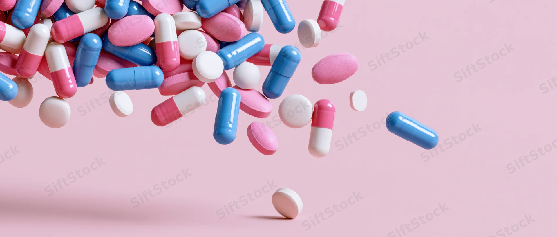 Assorted pharmaceutical pills and capsules scattered mid-air against a pink background