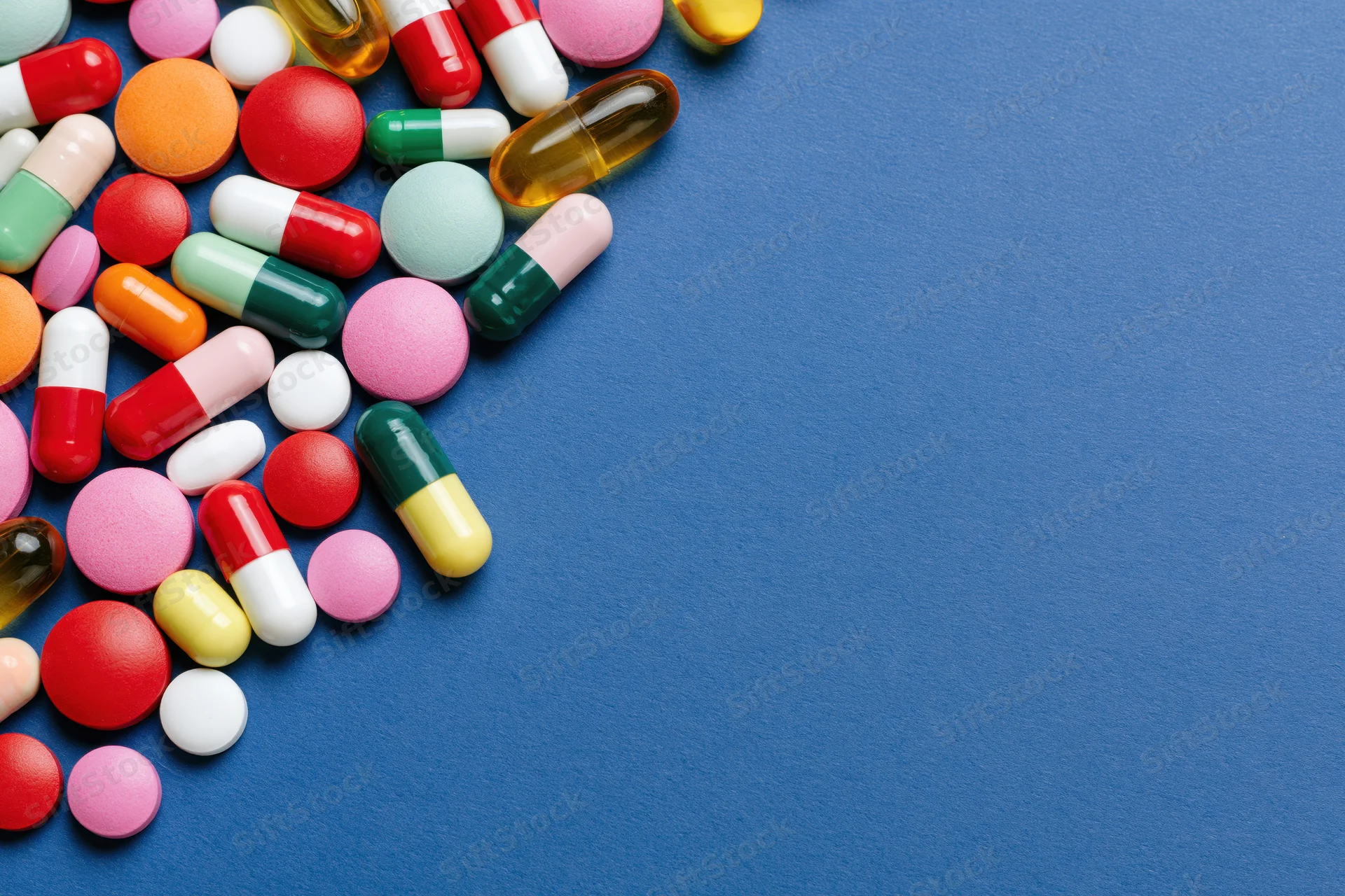 Assorted pharmaceutical pills capsules and gel tablets scattered on blue surface with copyspace