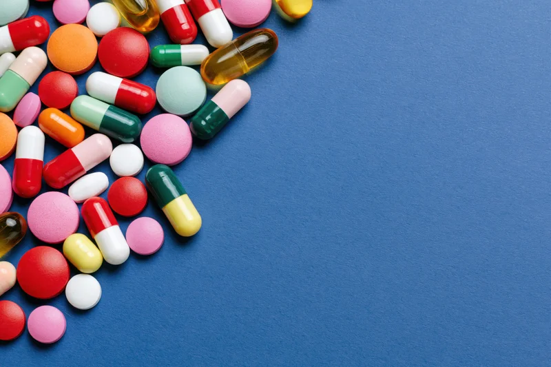 Assorted pharmaceutical pills capsules and gel tablets scattered on blue surface with copyspace
