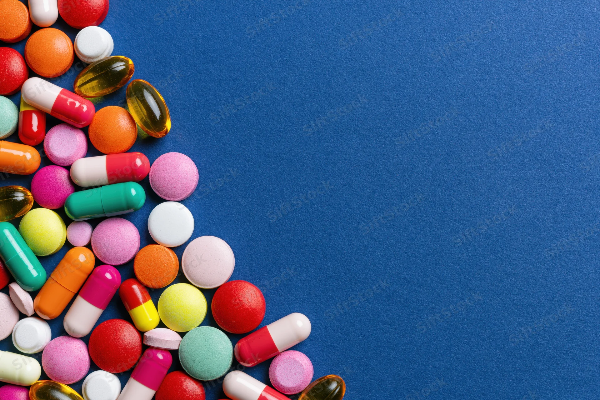 Assorted pharmaceutical pills capsules and gel tablets scattered on blue surface with copyspace