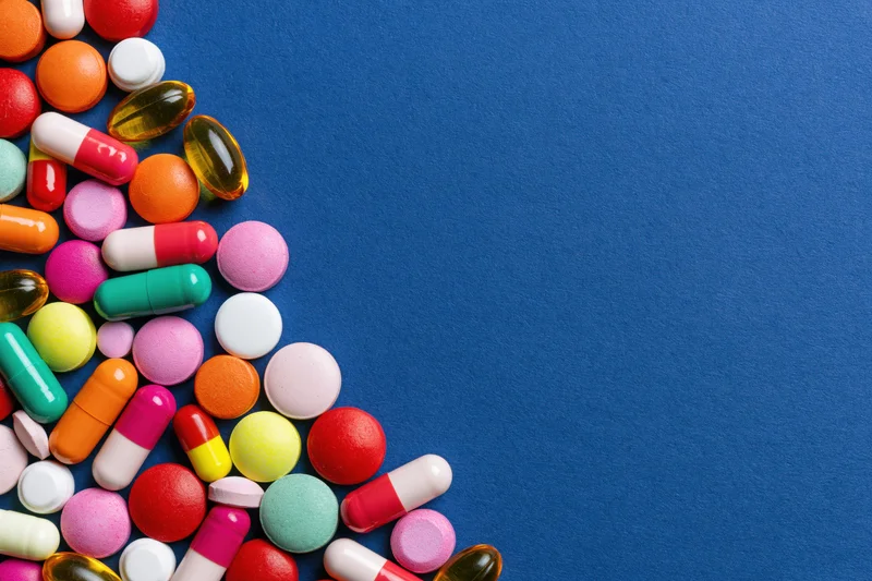 Assorted pharmaceutical pills capsules and gel tablets scattered on blue surface with copyspace