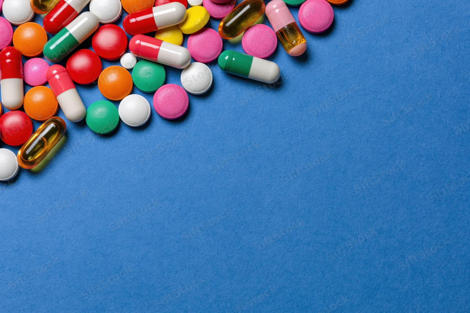 Assorted pharmaceutical pills capsules and gel tablets scattered on blue surface with copyspace