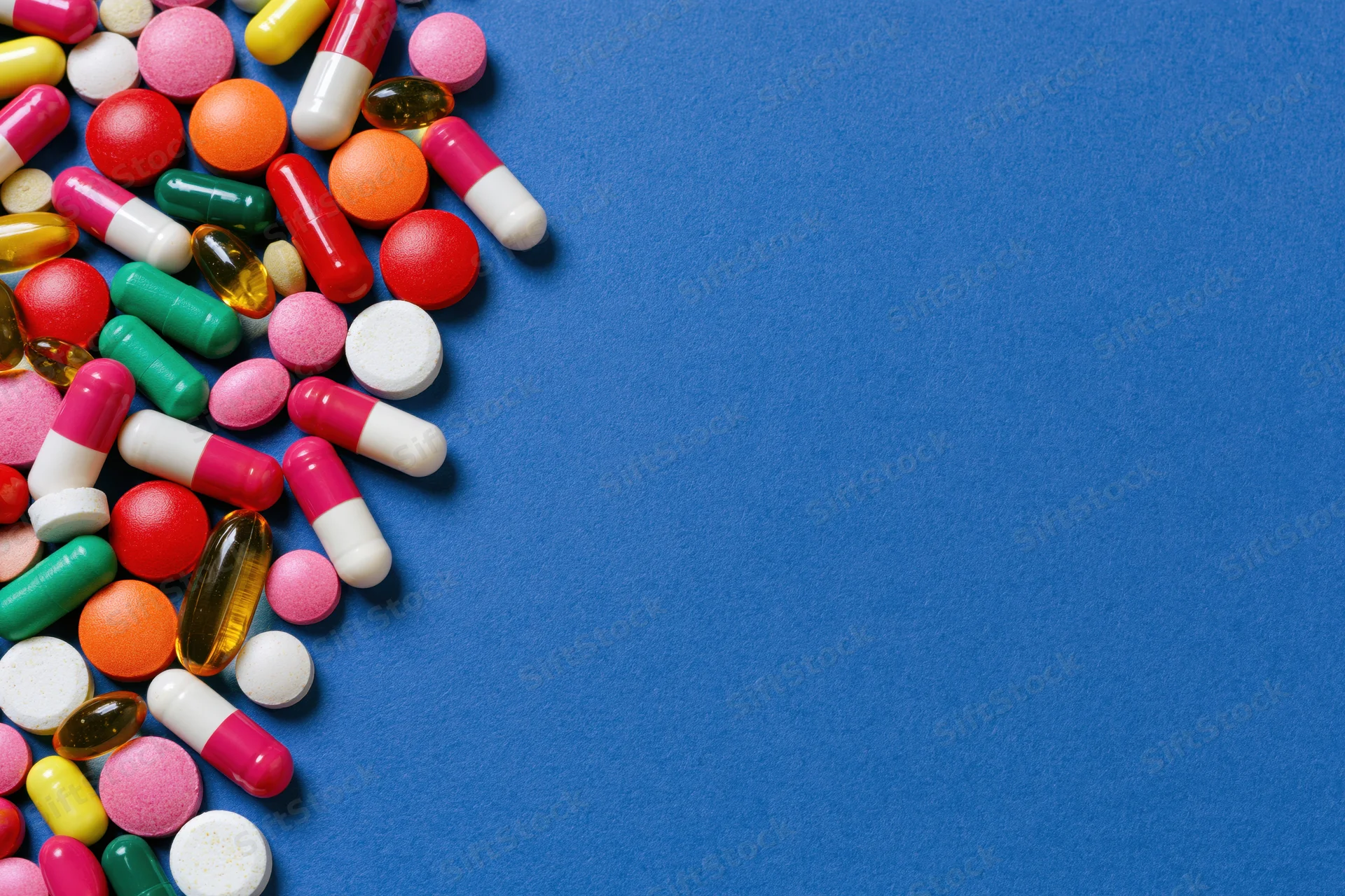 Assorted pharmaceutical pills capsules and gel tablets scattered on blue surface with copyspace