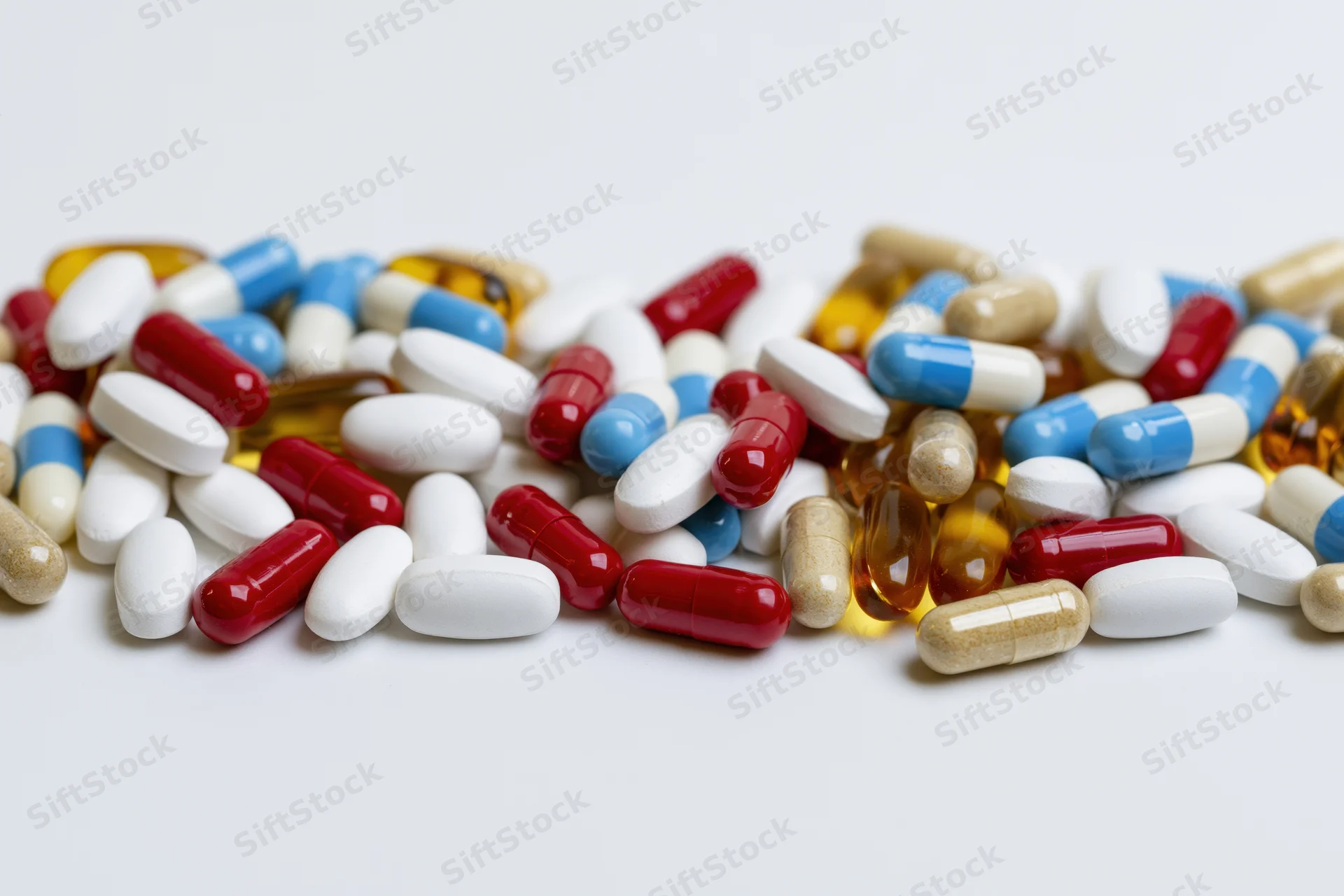 Assorted pharmaceutical pills tablets and capsules scattered on white surface