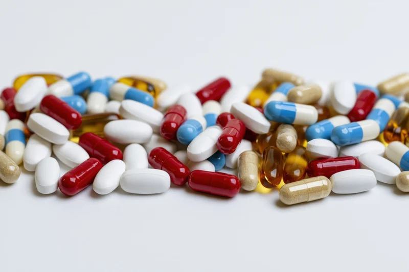 Assorted pharmaceutical pills tablets and capsules scattered on white surface