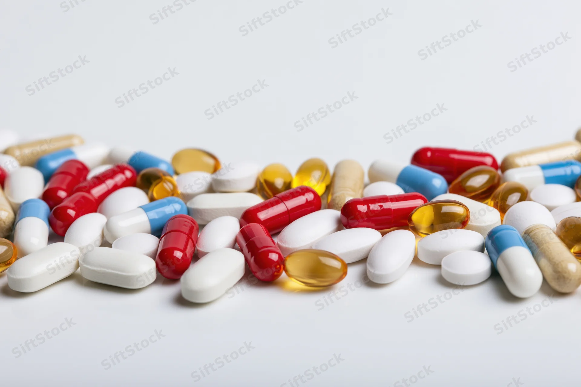 Assorted pharmaceutical pills tablets and capsules scattered on white surface