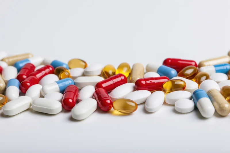 Assorted pharmaceutical pills tablets and capsules scattered on white surface