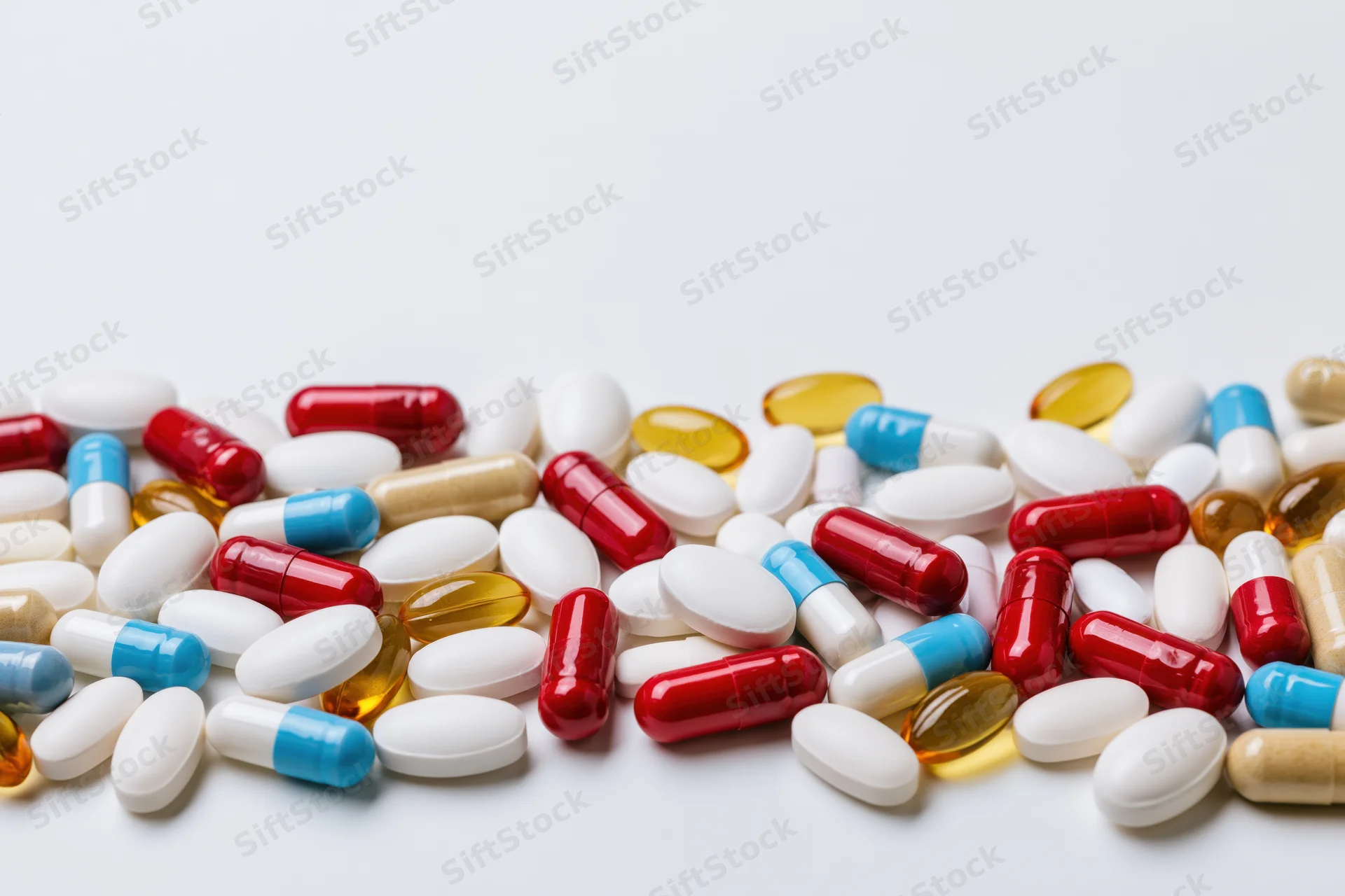 Assorted pharmaceutical pills tablets and capsules scattered on white surface