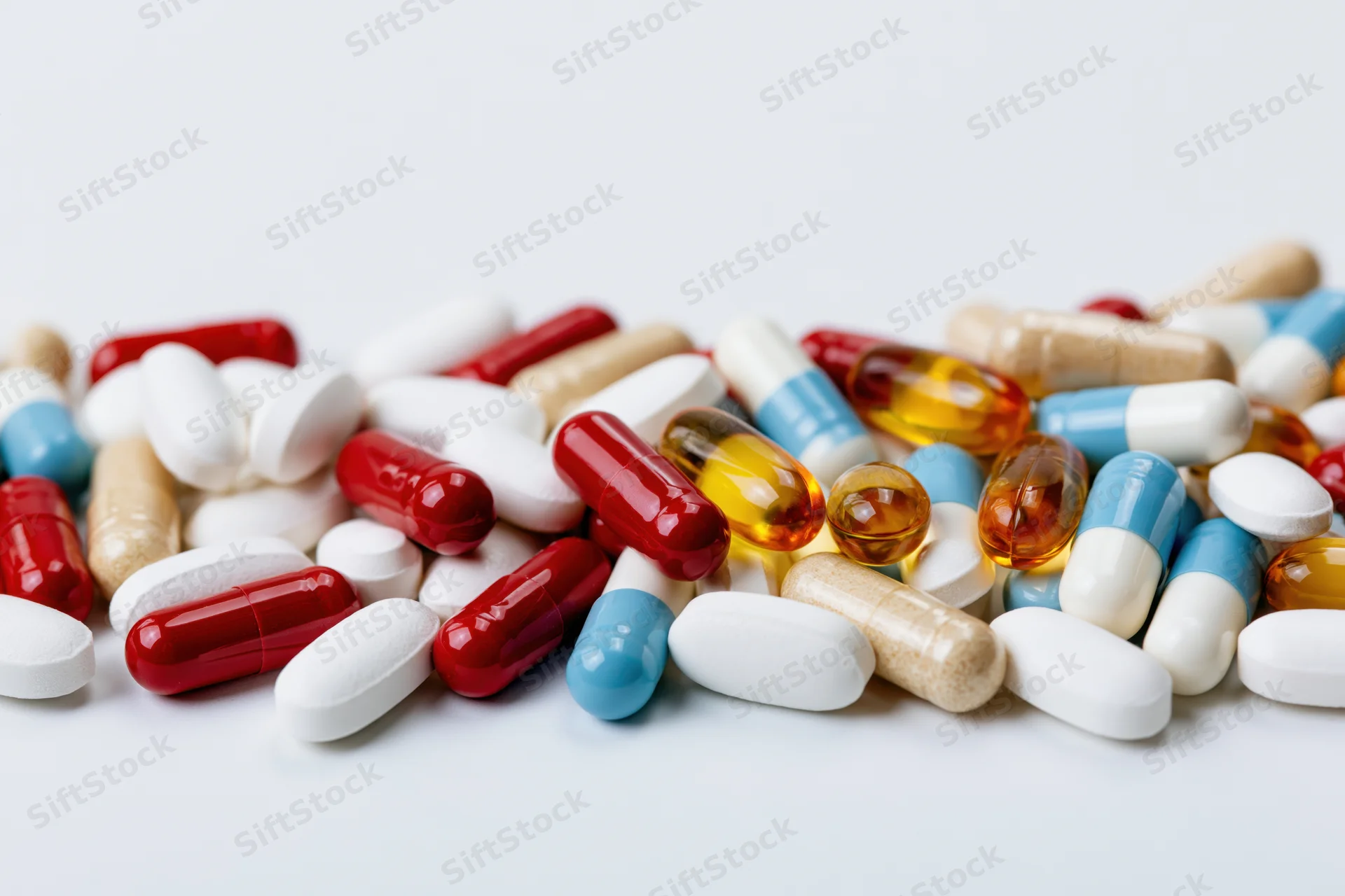 Assorted pharmaceutical pills, capsules and tablets scattered on a white surface