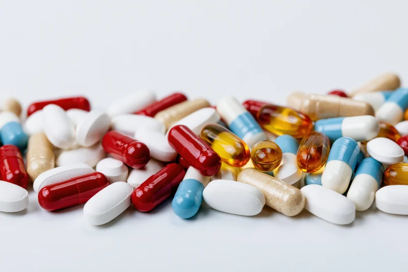 Assorted pharmaceutical pills, capsules and tablets scattered on a white surface